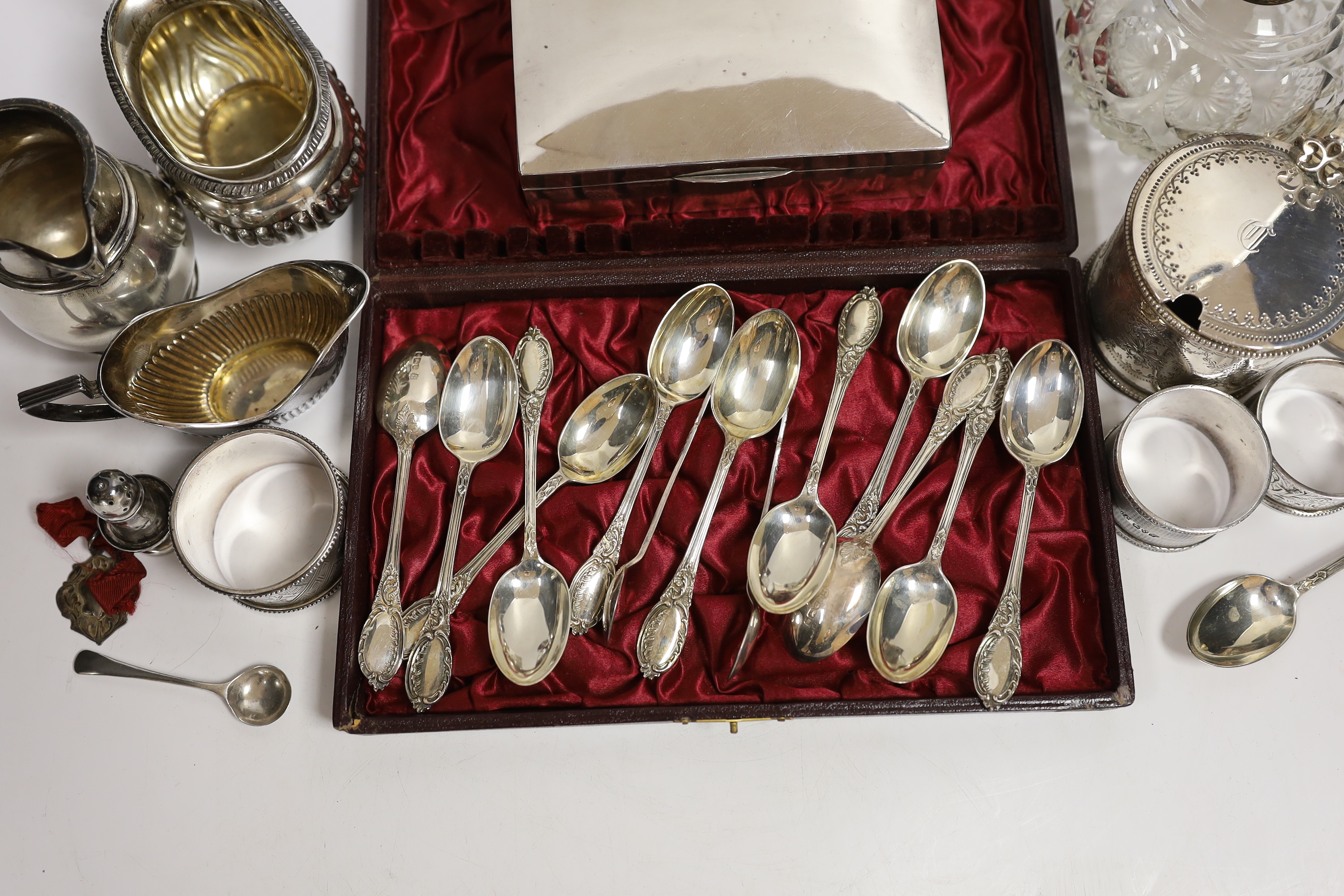 A Victorian silver mustard pot (no liner), a cased set of twelve silver teaspoons and tongs, two silver cream jugs, mounted glass scent bottle, napkin rings etc.